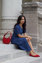 a lady wears a denim dresss with red ballet flats and handbag